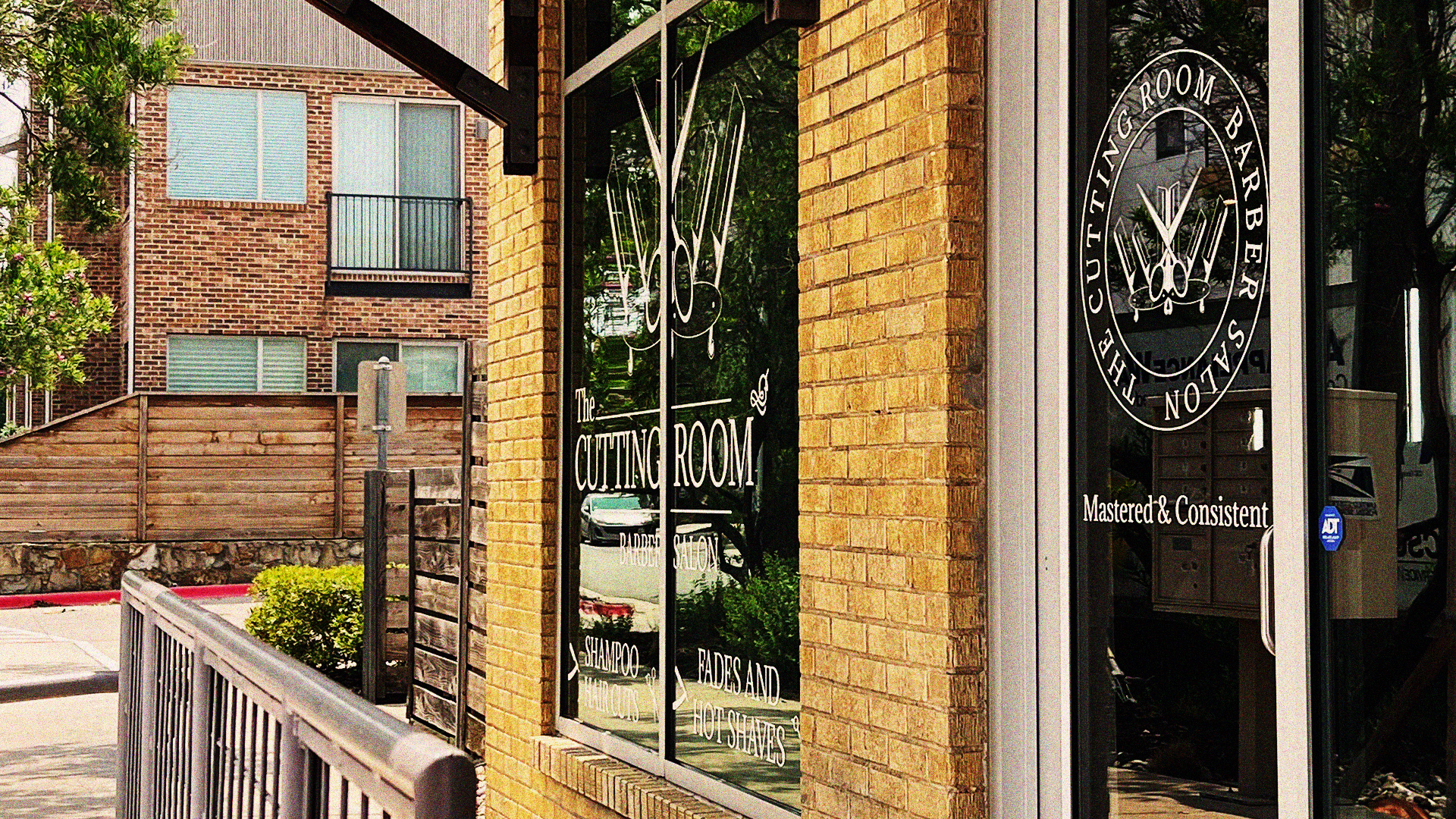 The Cutting Room storefront sits on a street corner with apartments and a wooden fence in the background.