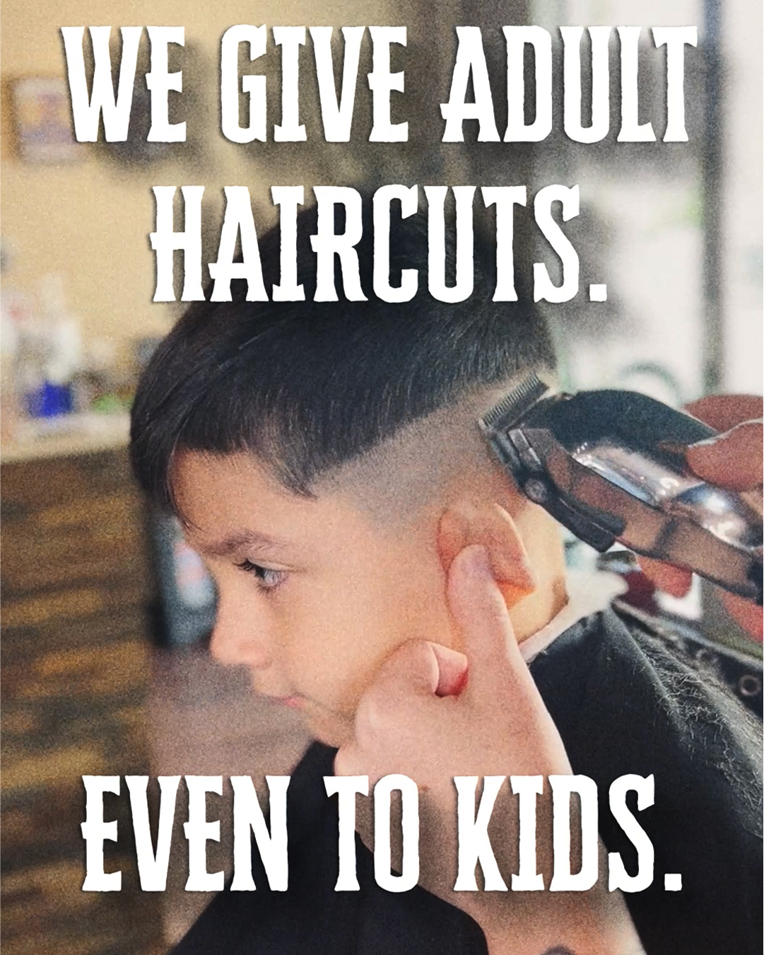 A child gets a haircut. At the top of the picture is the words, “We give adult haircuts.” Below that it says, “Even to kids.”